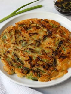 a white plate topped with an omelet next to a bowl of dipping sauce