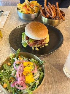 a table topped with two plates filled with food next to bowls of fries and salad