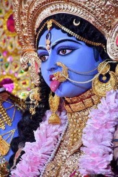 a close up of a person with blue makeup and gold jewelry on their face, wearing an elaborate headdress