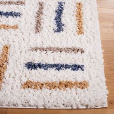 a white rug with blue, yellow and brown designs on the bottom is laying on a wooden floor