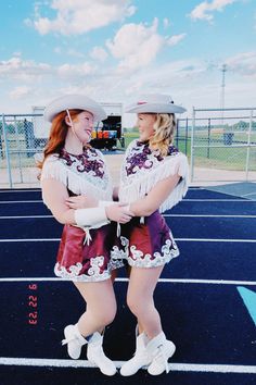 two women in short skirts and cowboy hats are standing on a parking lot with their arms around each other