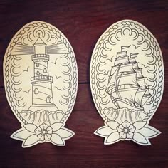 two decorative plates with an image of a ship and a lighthouse on them, sitting on a wooden surface