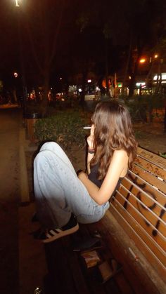 a woman sitting on top of a wooden bench next to a street light at night