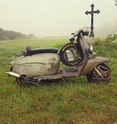 an old scooter sitting in the grass with a cross on it's back