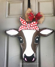 a door hanger with a cow wearing a red bow on it's head