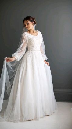 a woman in a white wedding dress with a veil on her head and hands behind her back