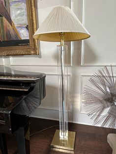 a lamp sitting on top of a wooden floor next to a piano and framed artwork