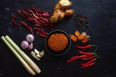 various vegetables and spices on a black surface with one red pepper, the other yellow