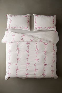 a bed with white sheets and pink bows on the comforter, along with two pillows