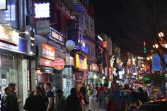 many people are walking down the street in front of stores and businesses at night time