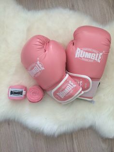 two pink boxing gloves sitting on top of a white fur covered floor next to a rubber pad