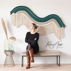 a woman sitting on a bench in front of a wall hanging with fringes and flowers