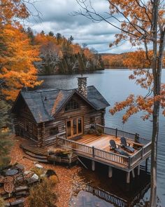 a wooden house sitting on top of a lake surrounded by fall foliage and trees in the background