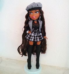 a doll with long brown hair wearing a black and white plaid dress, hat and boots