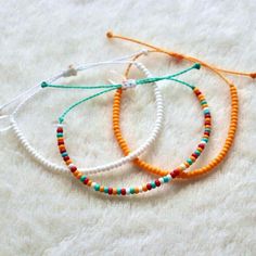 three bracelets with different colored beads are on a white surface and one has an orange string