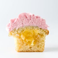 a cupcake with pink frosting and a bite taken out of it on a white surface