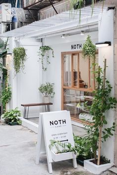 a white sign sitting in front of a building with lots of plants growing out of it