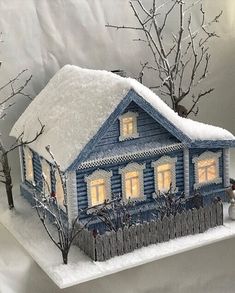 a small blue house with snow on the roof and trees in front of it, lit up at night