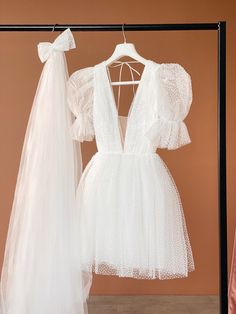 two white dresses hanging on clothes racks in front of a pink wall and one is wearing a veil