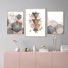 three abstract paintings hang on the wall next to a pink cabinet and white vases