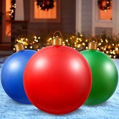 three christmas ornaments sitting on the ground in front of a house with holiday lights behind them