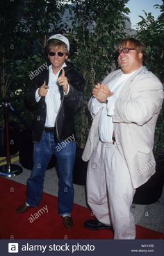 two men in white suits and sunglasses standing on a red carpet with one holding an umbrella