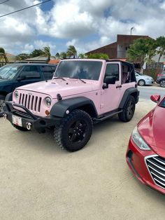 a pink jeep parked next to a red car