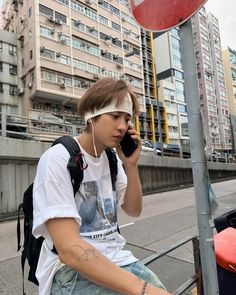 a young man sitting on the curb talking on his cell phone and listening to music