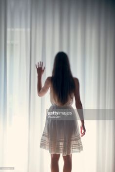 a woman standing in front of a window with her hands out to the side,