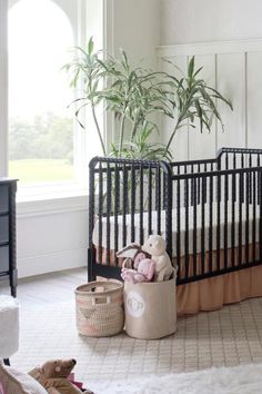 a baby's crib in a white room with a potted plant and stuffed animals