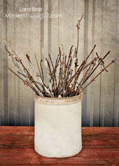 a white vase filled with twigs on top of a wooden table