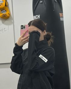 a woman taking a selfie in front of a punching bag with her cell phone