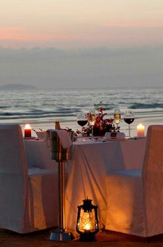 a table set up on the beach with wine glasses and candles