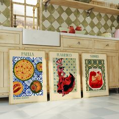 three framed art prints on the wall in a kitchen with tile flooring and cabinets