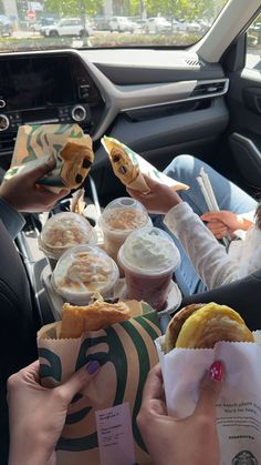 some people are sitting in the back seat of a car eating sandwiches and drinking coffee