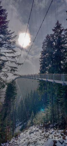 the sun shines through the clouds above a suspension bridge over a snow covered river