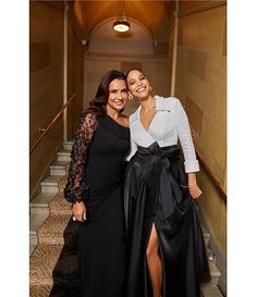 two women standing next to each other in front of some stairs wearing black and white dresses