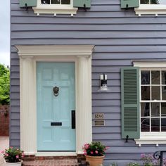 a blue house with green shutters and two potted plants on the front porch