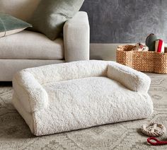 a dog bed sitting on the floor next to a couch with pillows and a pair of slippers