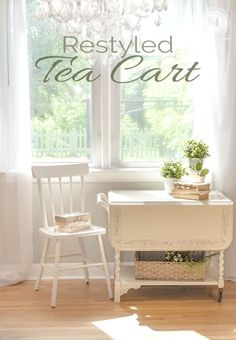 two white chairs and a table in front of a window with a chandelier