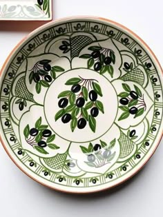 a green and white bowl sitting on top of a table next to a plate with black olives