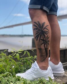 a man with a palm tree tattoo on his leg, standing next to some plants