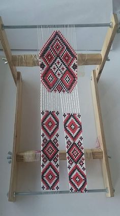 a weaving machine with red and black beads hanging from it's sides on a wooden stand