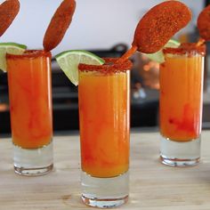 three glasses filled with orange liquid and garnished with lime wedges on top