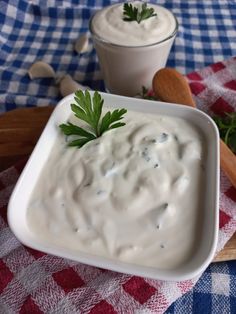 a white bowl filled with ranch dressing next to two wooden spoons on a checkered tablecloth