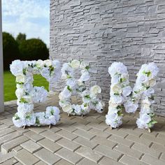 the word mom spelled with white flowers in front of a brick wall and grass area