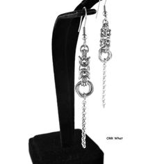 a pair of earrings with chains hanging from it's earring hooks on a black velvet stand