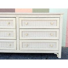 a white wicker dresser with drawers and knobs on the bottom, against a multi - colored wall