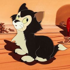 a black and white cat sitting on top of a wooden floor next to a red wall