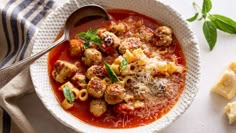 a bowl filled with pasta and meatballs on top of a white table next to some parmesan cheese